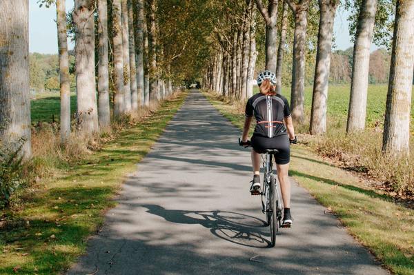 Frau fährt mit dem Fahrrad auf einer von Bäumen gesäumten Strecke